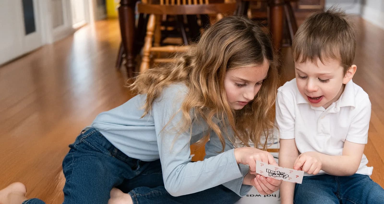 A big sister and little brother playing an emotion card game together at home